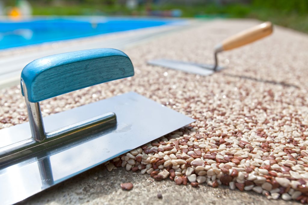 hladítka urovnávají kamínky na betonovém chodníku okolo bazénu